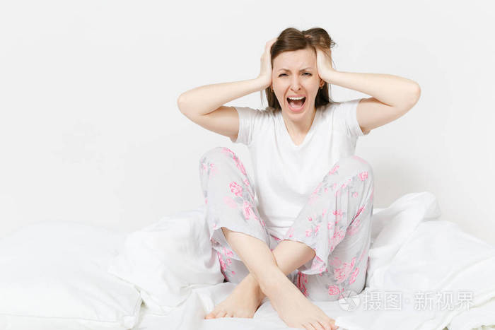 紧张的疯狂的年轻尖叫的女人坐在床上白色床单枕头毯子用手震撼女性捂