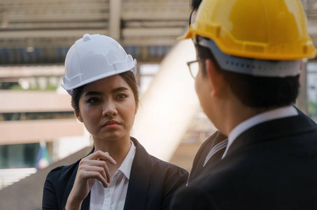 两名年轻的亚洲妇女和商业男子或工程师，戴着白色和黄色安全帽，规划施工现场的新项目建设计划商业建设和行业概念