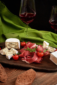 意大利火腿, 意大利香肠, 长方形切片, 西红柿和星期六质朴的木板, 黑色背景的两杯红酒