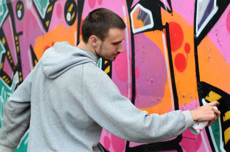 一个穿着灰色连帽衫的年轻人在下雨天在墙上画了粉红色和绿色的涂鸦