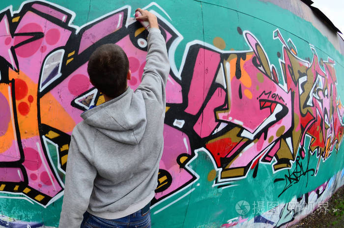 一个穿灰色连帽衫的年轻人在雨天在墙上画了粉红色和绿色的涂鸦.