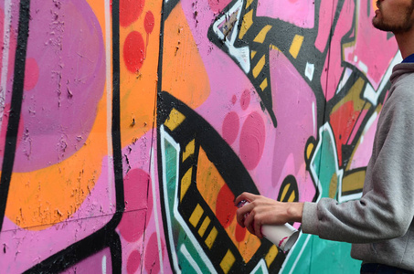 一个穿着灰色连帽衫的年轻人在下雨天在墙上画了粉红色和绿色的涂鸦