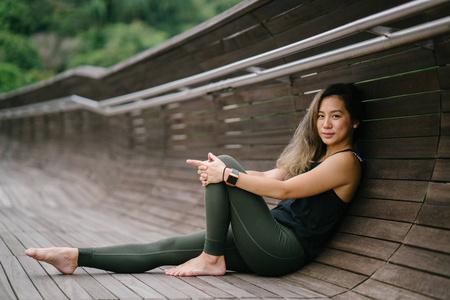 周末，新加坡一个郁郁葱葱的绿色公共公园的一座桥上，一位穿着运动型活动服装的迷人的中国年轻亚洲女性的肖像。