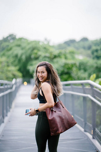 一位迷人的中国年轻亚洲女性的肖像，周末在新加坡的绿色公共公园穿着运动的活动服装，带着袋子。