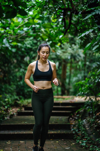 迷人的年轻中国亚裔妇女，穿着运动的活动服装，在新加坡的一个公共公园的小径上跑步，在周末锻炼。