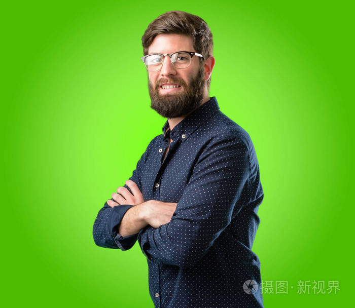 年轻的时髦男人长着大胡子交叉着双臂自信而快乐在绿色的背景下笑着