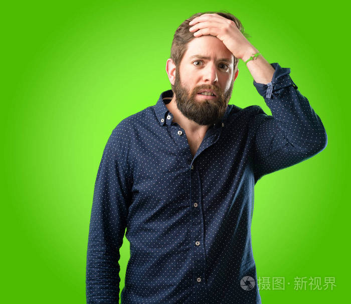 一位留着大胡子惊恐不安焦虑不安的年轻潮人在绿色的背景下不知所措