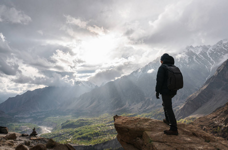 山峰阳光一个背着背包的人站在山峰上,阳光透过多云的天空.