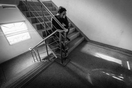 情绪低落的人在楼梯上坐着，在消防通道或建筑楼梯上，光线较低，有戏剧性的场景概念
