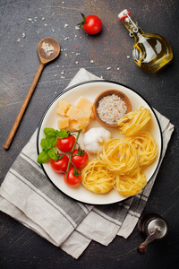 传统意大利面食的原料。 未煮熟的生TagliatelleBolognesi Parmesan奶酪橄榄油大蒜罗勒叶胡椒樱桃番茄在旧