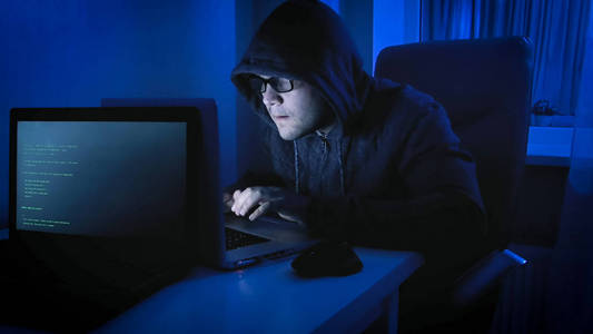 年轻的黑客在头戴头套工作的程序代码在夜间