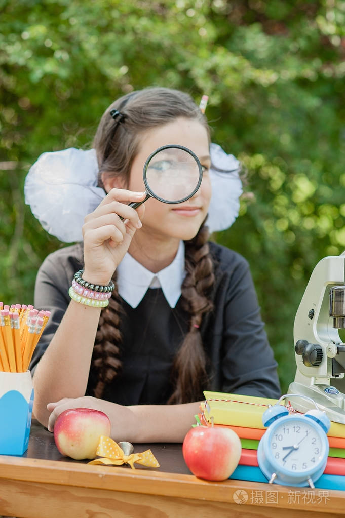 一个美丽的年轻女孩的肖像看着放大镜和坐在办公桌上