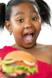 特写表情的小非洲女孩的脸，张开嘴，大眼睛要吃汉堡包。Kid拿着肉汉堡婴儿的脸孤立在白色的背景上。