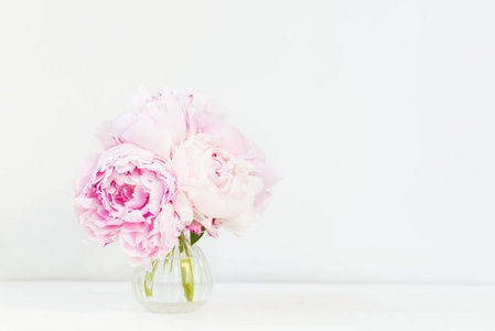 新鲜的一束粉红色牡丹在小花瓶上的浅色背景。 卡片概念复制空间文本