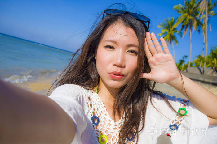 妇女的自画像20s 在异国风情的热带海滩上拍摄自拍照片与手机摄像机