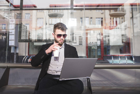 忙碌的人坐在一台笔记本电脑后面的公交车站和喝咖啡。商业人在公共场所工作。忙碌的人没有时间做这项工作。