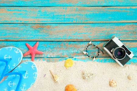 海滩背景。 顶部的海滩沙维与拖鞋海星贝壳珊瑚复古卡拉和手镯贝壳制成的蓝色木制背景。 夏季概念复古风格。