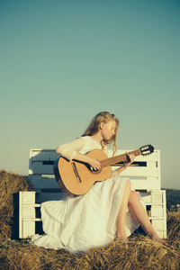 女吉他弹奏者演奏音乐音乐会。时尚音乐家在白色礼服在阳光自然。白化女孩持有声学吉他, 弦乐器。女人在木凳上弹吉他