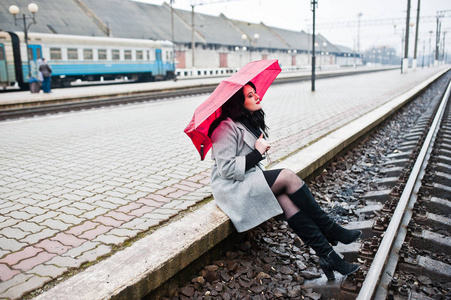 穿灰色大衣的黑发女孩在火车站的红色雨伞