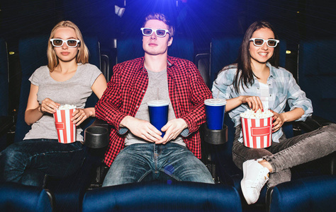 电的家伙年轻人坐在电影院的椅子上.他们戴眼镜看电影.