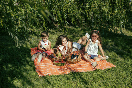 可爱的幸福的家庭野餐铺上绿草母亲和孩子，温暖的夏季假期关闭起来，弟弟和妹妹