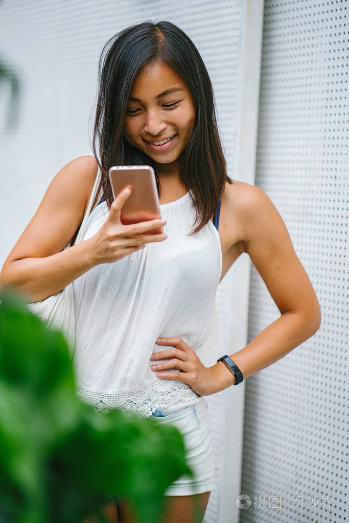 运动色调和晒黑的中国亚洲女孩微笑,当她在她的手机短信在一天.