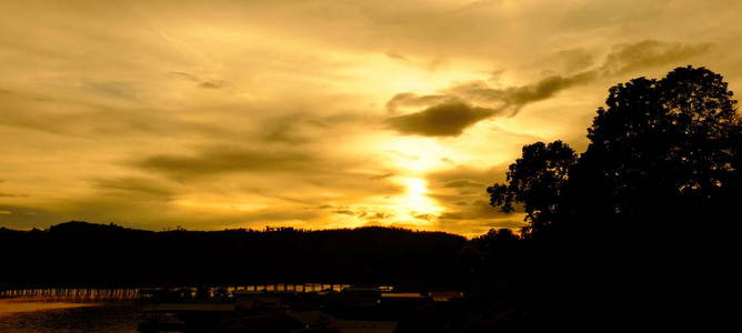 当太阳在傍晚前落下时，五彩缤纷的天空。泰国SangklaburiKhaoLaem水坝附近的河流和大坝周围社区的游客和景观。5月2