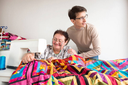 家庭关系职业商业观念。有一个年轻而迷人的在他的祖母身边, 她正在缝制巨大华丽的毯子缝制明亮的织物