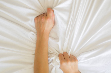 女性在白床上的手指，女性在狂喜的感觉和情感概念中拉着白色床单的手