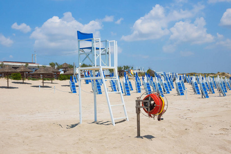 海洋救生员的椅子，靠在阳光和雨伞的背面。 背景蓝天白云在阳光明媚的夏日。 游客安全概念