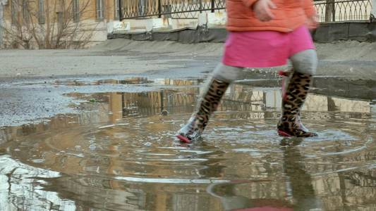 小漂亮女孩雨后跳在水坑上