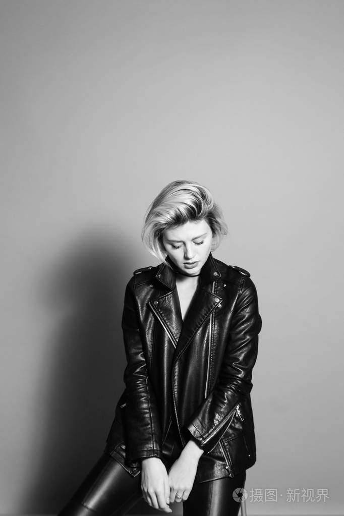 一个金发美女的特写照片,穿着黑色机车夹克,悲伤地低头,背景是普通的