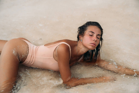 一个美丽的女孩与的身体在沙滩上的白色沙子的肖像。穿着泳装的年轻女子在国外的暑假里晒日光浴。沙漠岛上的迷人模特
