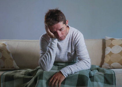年轻的悲伤和绝望的男人坐在客厅沙发上,沮丧和压力,担心问题,感到