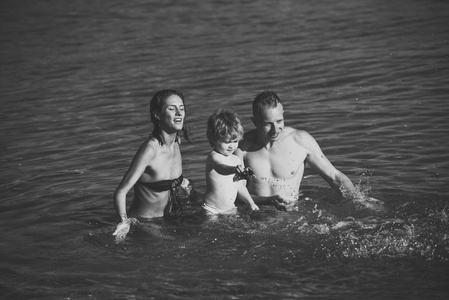 父亲和母亲在海里和儿子一起游泳。全家人一起共度时光, 享受快乐。可爱的儿童男孩玩玩具在海洋, 海, 与父母。家庭度假的概念。阳光