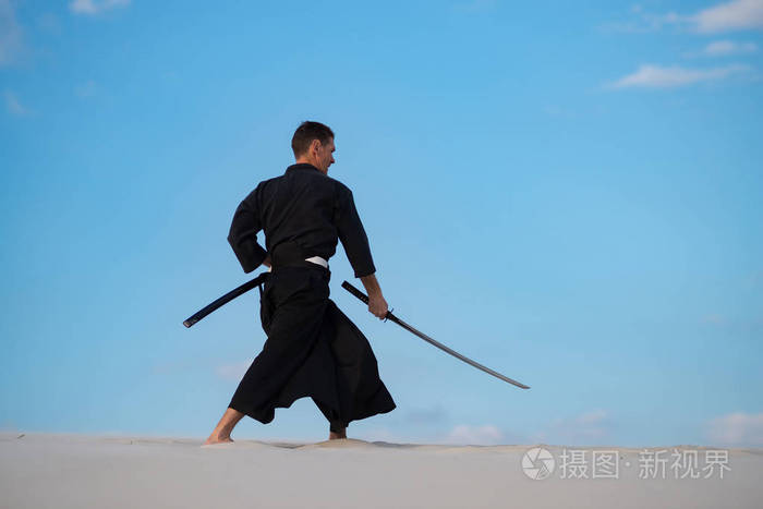 专注的人穿着传统的日本衣服,手里拿着剑,正在沙漠中训练武术,日落时
