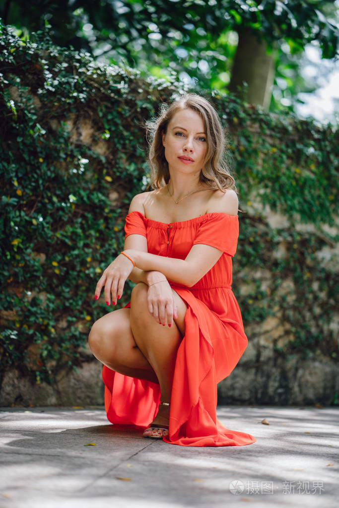 一个年轻迷人的欧洲女人的肖像穿着橙色的夏季礼服摆姿势她金发碧眼