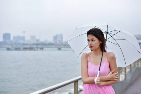 假日概念。 美丽的女孩在海滩上拿着雨伞。 当下雨时，美丽的女孩感到寒冷。 美丽的女孩高兴地笑着。