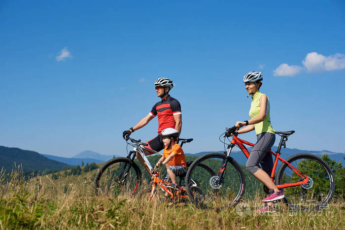 年轻的现代家庭游客骑自行车在草山上,远山观背景,积极的生活方式
