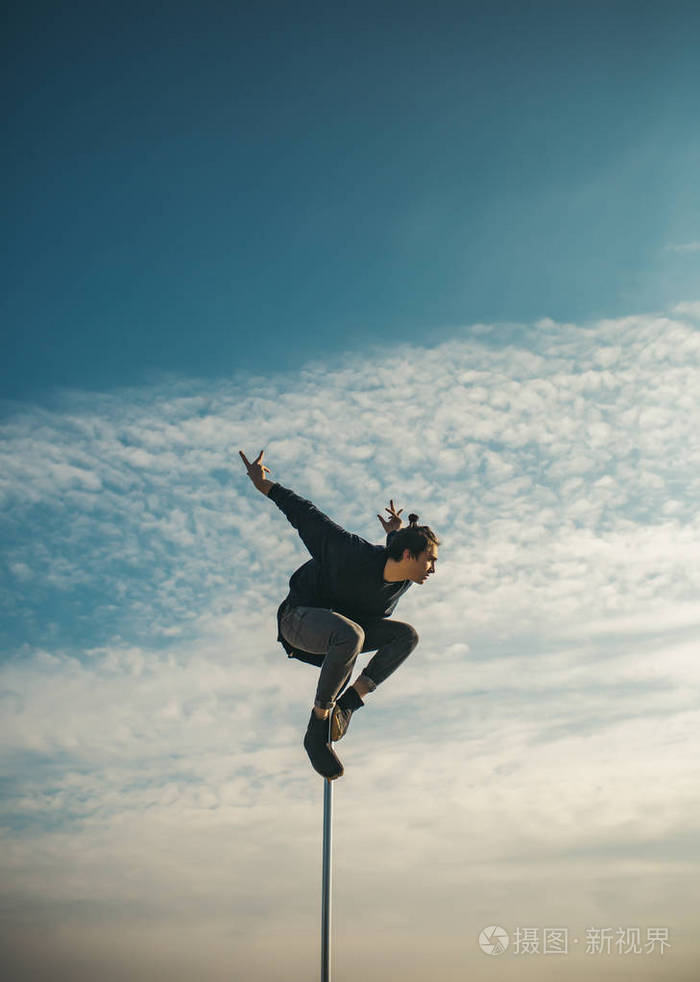 性感的男人在蓝天背景上飞翔. 年轻人在塔上跳舞. 钢管舞运动.