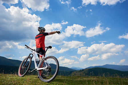穿运动服和头盔的职业男性自行车手站在山顶上，在夏天阳光明媚的日子里，积极的生活方式和户外运动理念指向蓝天