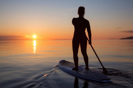 桨冒险在一个明亮而充满活力的日落中,划桨板上的冒险女孩正在滑行.