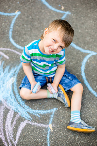 可爱的男孩和女孩在公园的人行道上用粉笔画画。 儿童暑期活动。 用蓝色粉笔在路上创造性地画一个孩子。
