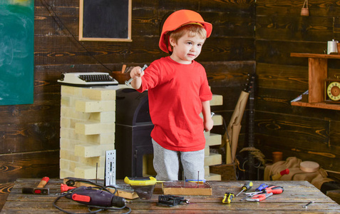 幼儿在保护硬帽子, 头盔在家里的车间。孩子可爱和可爱的玩工具, 作为建设者或修理工, 修理或就要手工制作。童年的概念。小男孩扮演