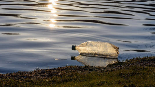 日落时沿岸线漂浮的单个塑料水瓶垃圾照片