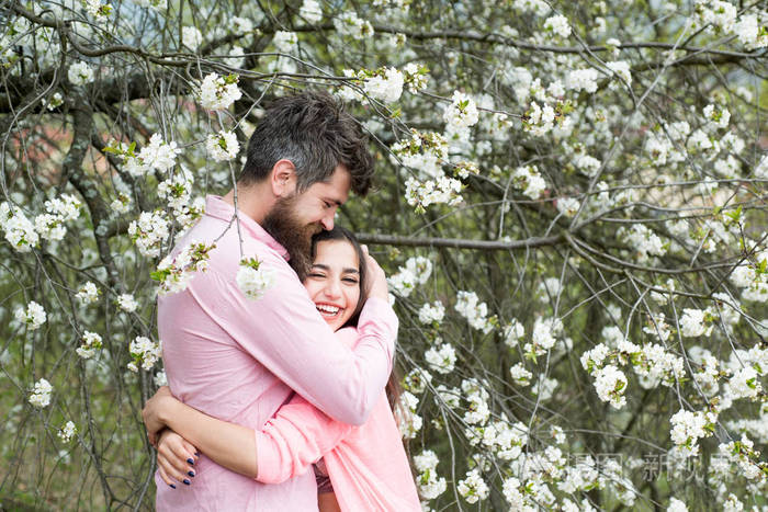 春季约会的概念情侣拥抱在盛开的树木附近春天男人和女人拥抱在盛开的