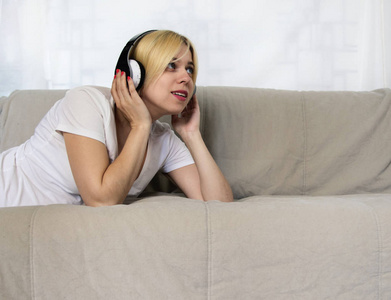 戴着耳机的漂亮年轻女人躺在沙发上,闭着眼睛听音乐或听音频书.