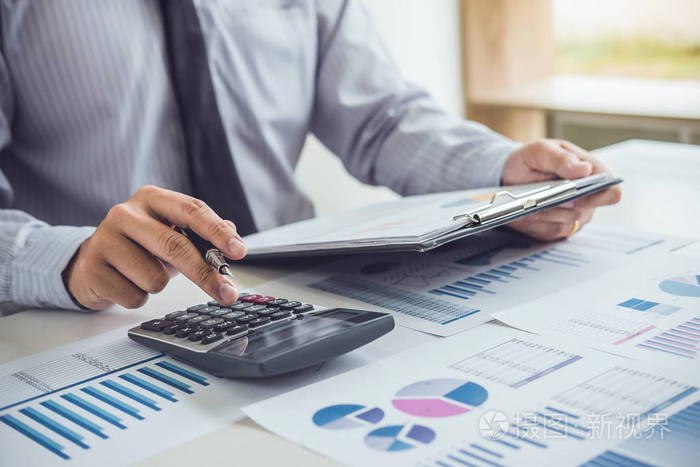 商务人员或会计人员在计算器上进行财务投资,并在财务文件数据图上