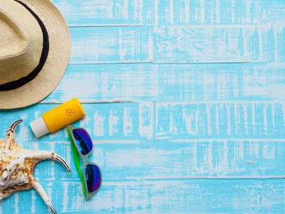 海滩配件，包括太阳镜，防晒霜，帽子，海滩和贝壳，明亮的蓝色木制背景，为暑假和假期的概念。