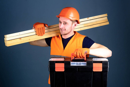 专业木工概念。木匠工人建设者木工在笑脸上扛着木梁。男子头盔, 硬帽子持有工具箱和木梁, 灰色背景